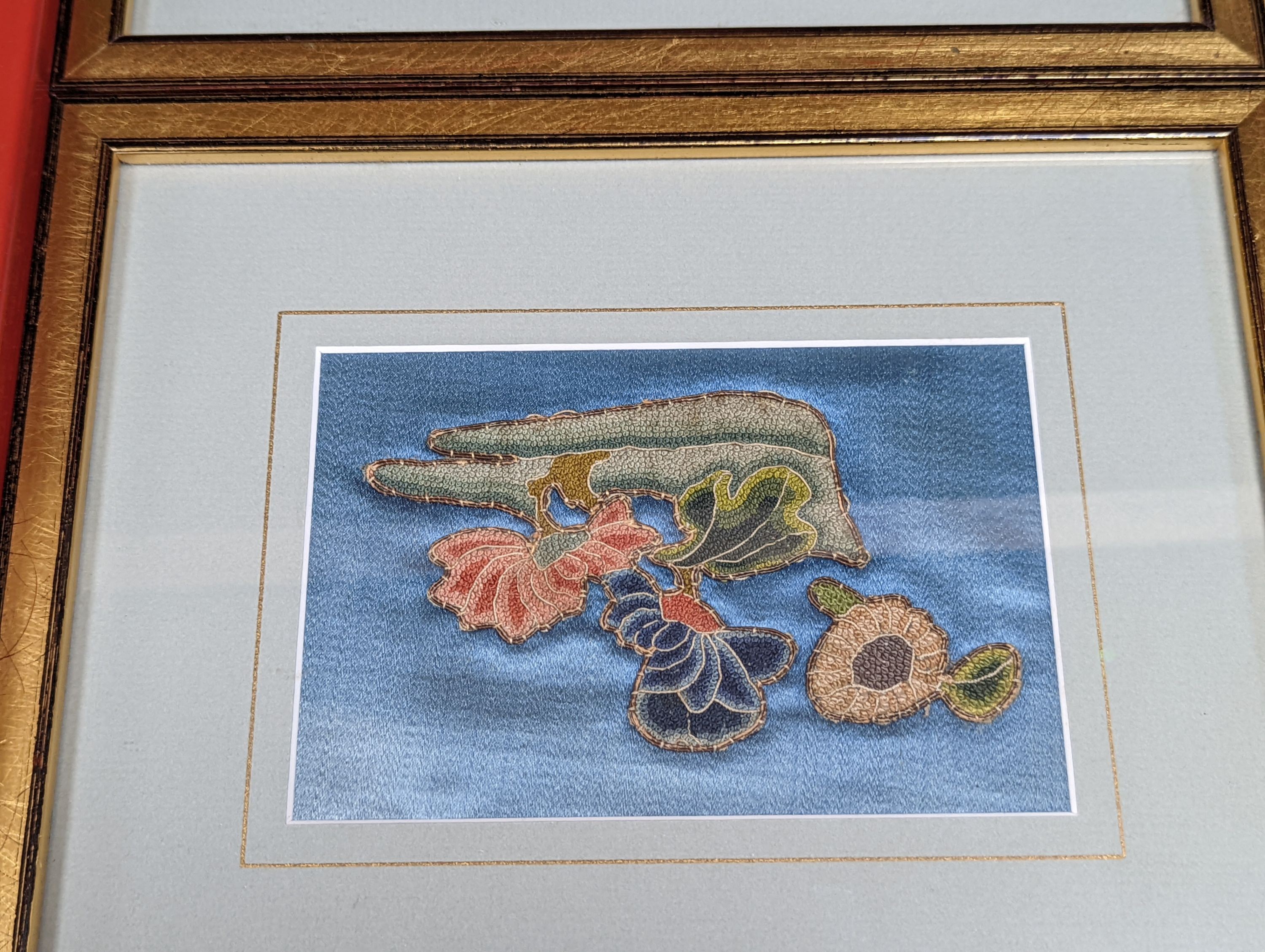 A set of four Chinese silk embroidered motifs, a pair of floral silk motifs and a later pair f sleeve bands, all framed